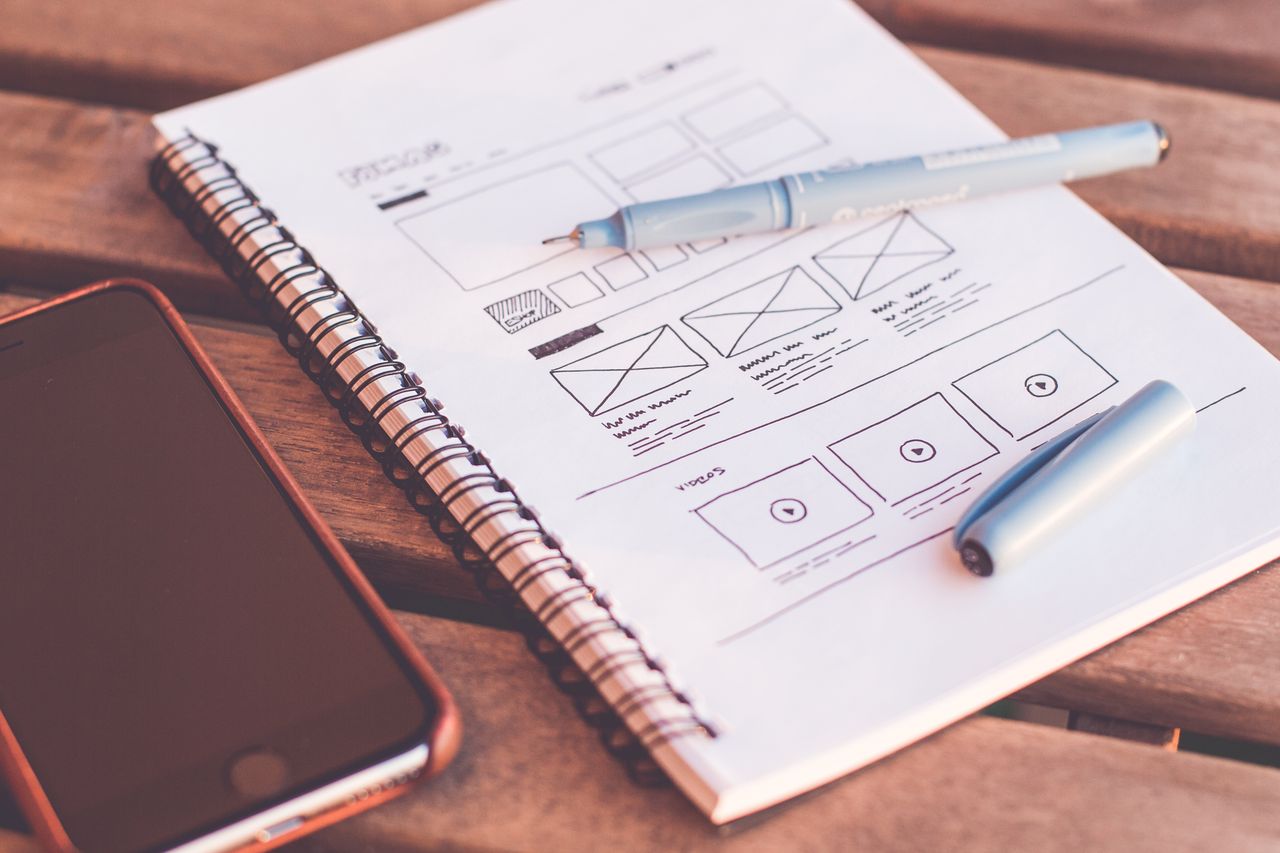 Detail notebooku s wireframe náčrty a smartphonem na dřevěném stole.
